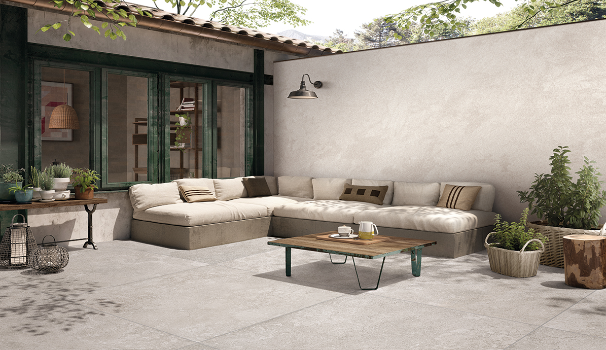 Bequeme beige Eckcouch und Holztisch auf einer sonnigen Terrasse umgeben von Pflanzen