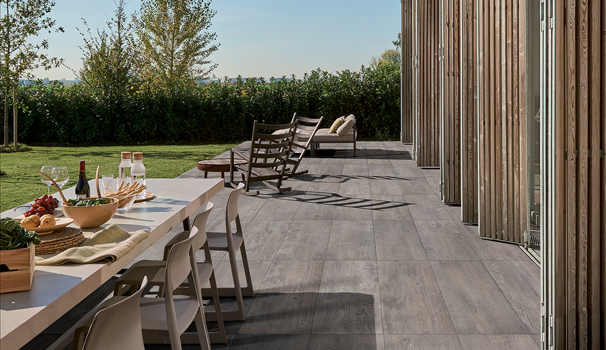 Terrasse mit Tisch gedeckt für ein Essen im Freien, umgeben von Liegestühlen und grüner Hecke