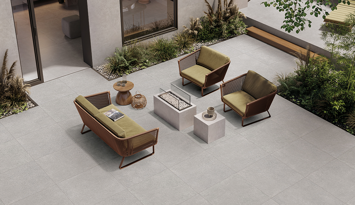 Draußen aufgestellte Terrassenmöbel mit grün gepolsterten Stühlen und Sofa um einen modernen Feuertisch, umgeben von Pflanzen und Steinen.