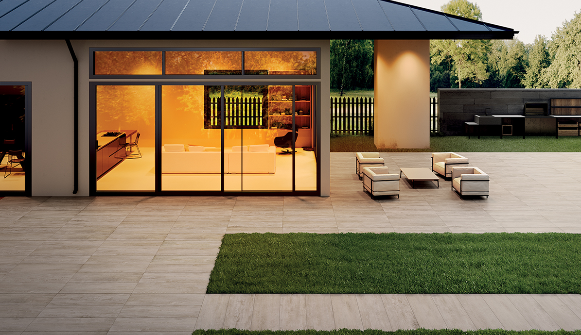 Eine moderne Terrasse mit eleganten Gartenmöbeln und einem Blick ins Interieur, das in warmen Lichtern erstrahlt. Im Hintergrund ist ein gepflegter Garten zu sehen.